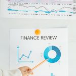 Close-up of financial analysis showing graphs, charts, and person pointing with pencil.